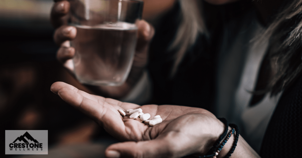 Woman holding a glass of water and variety of pills.