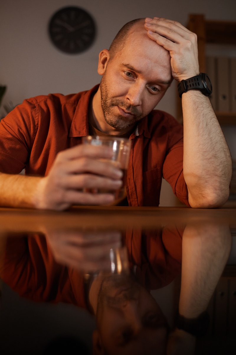 man holding glass of alcohol at table lookin sad