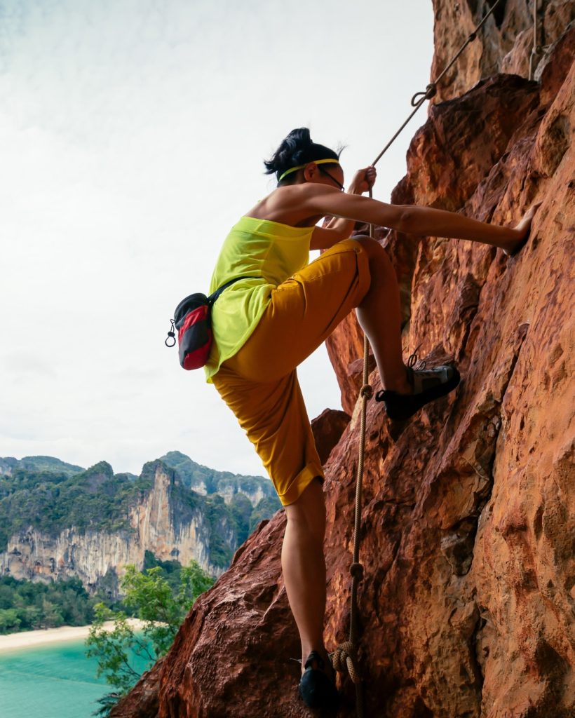 Woman rock climber climbing on seaside cliff