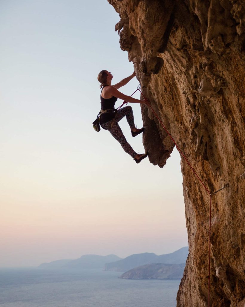 Young woman climbing challenging route at sunset